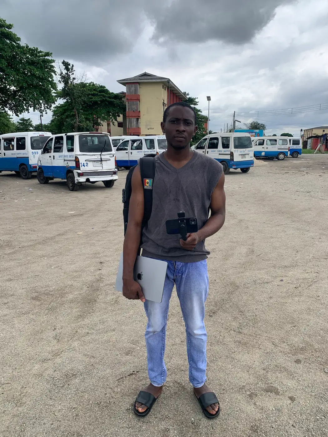 odii standing at the uniport motor park with a backpack and a phone on a stick